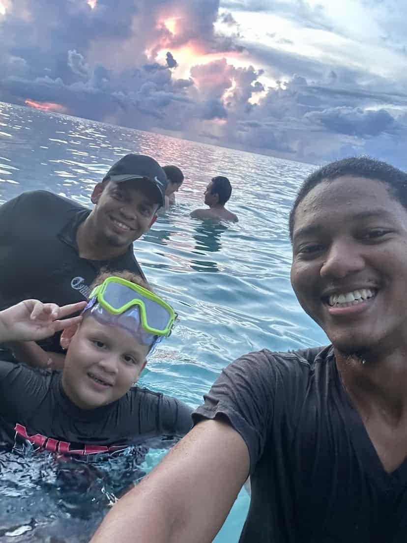 Captain Julio with a young guest in a snorkel mask and family in the water off Roatán at sunset